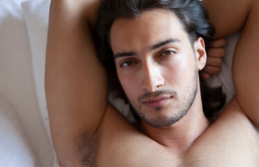 Fototapeta premium Portrait of a long haired handsome man lying on the bed and looking at camera