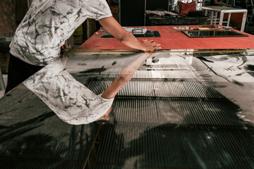 An unrecognizable carefully measures a sheet of glass using a ruler in a craft workshop, ensuring...