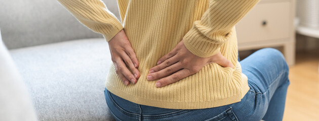 Pain body muscles stiff, suffer asian young woman painful with back pain, back ache sitting on sofa...
