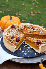 top view of pumpkin pie on a black tray stands on a wooden table with pumpkins and fall leaves