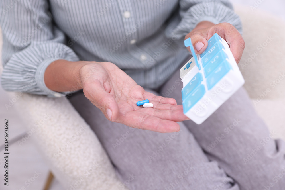 Poster Senior woman with pills and organizer in armchair at home, closeup