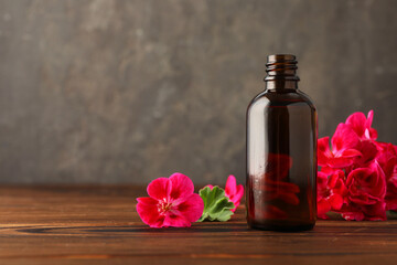 Geranium essential oil in bottle and beautiful flowers on wooden table, space for text