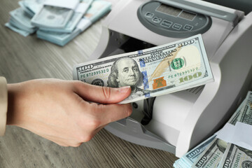 Woman using money counter machine at wooden table, closeup