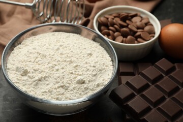 Flour, chocolate and egg for making dough on dark table, closeup