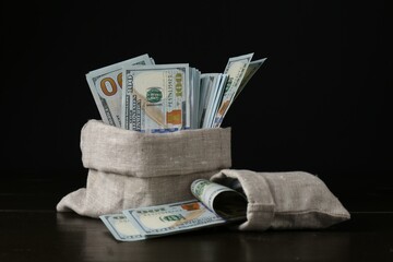 Dollar banknotes in sacks on wooden table against black background