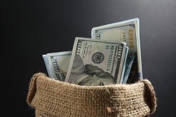 Dollar banknotes in burlap sack on dark background, closeup