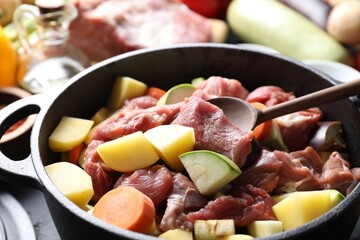 Cooking stew. Uncooked meat, vegetables and pot on black table, closeup