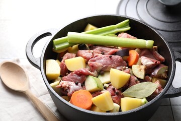 Cooking stew. Uncooked meat and vegetables in pot on white tiled table, closeup