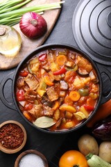 Delicious stew with vegetables in pot and ingredients on gray textured table, flat lay