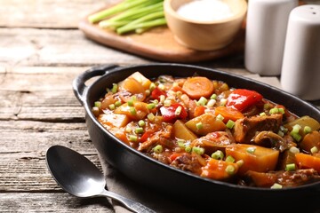 Delicious stew with vegetables in baking dish and spoon on wooden table, closeup