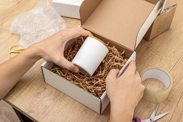 Man packs fragile candle or cup into box. Packaging of fragile items for delivery