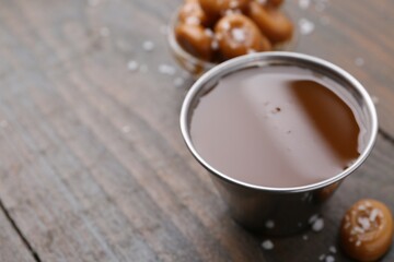 Tasty salted caramel in bowl and candies on wooden table, closeup. Space for text