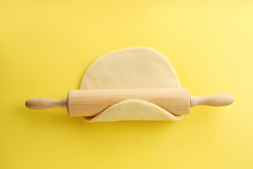 Cooking homemade pie. Raw dough and wooden rolling pin on yellow background, top view