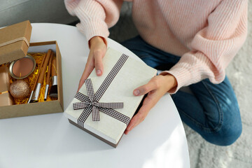 Woman holding Christmas gift boxes with makeup brushes and cosmetics at white table, above view