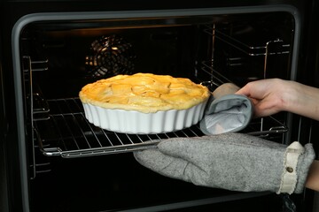 Woman putting homemade apple pie into oven in kitchen, closeup