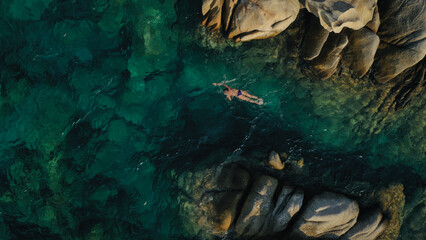 A woman gracefully swims through the crystal clear sea, her Sunlight dances on the surface,...