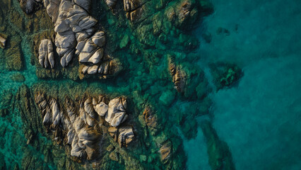 Aerial view of a serene coastal waterscape, where the dance of sunlight on the undulating waves meets the rugged embrace of rocky shores.