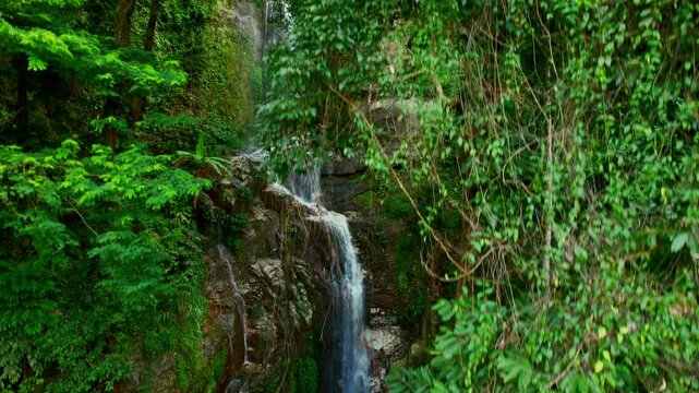 Aerial shot from up to down of the Huai Tueng Thao waterfall flowing down a high rocky cliff, Thailand