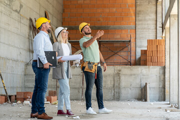 A female architect and construction managers work together on-site, discussing  and coordinating to...