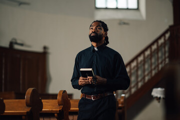 Young priest holding bible looking up in church