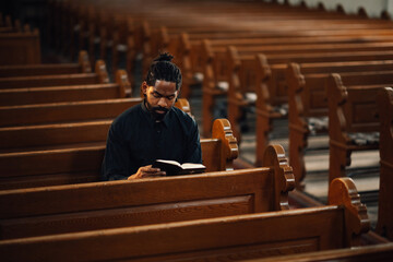 Young priest reading holy bible sitting in church pew