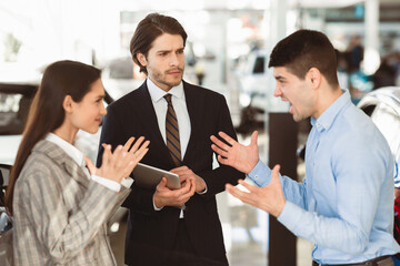 Car Seller Looking At Couple Having Quarrel About Buying Too Expensive Car In Dealership Showroom. Selective Focus