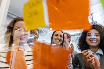 Brainstorming of office coworkers. Smiling team members participate in a brainstorming session, viewed through glass covered with colorful sticky notes.