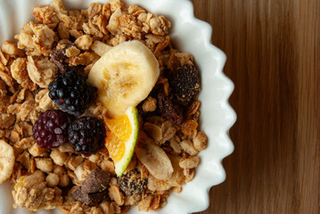 A decorative bowl filled with oat flakes, topped with slices of ripe banana, juicy tangerine segments, and fresh blackberries. 