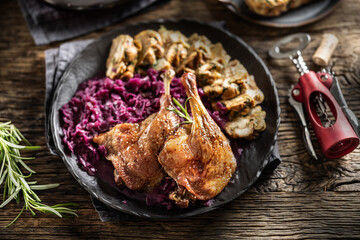 Portion of roast duck leg red cabbage homemade dumplings on plate and red wine on the background