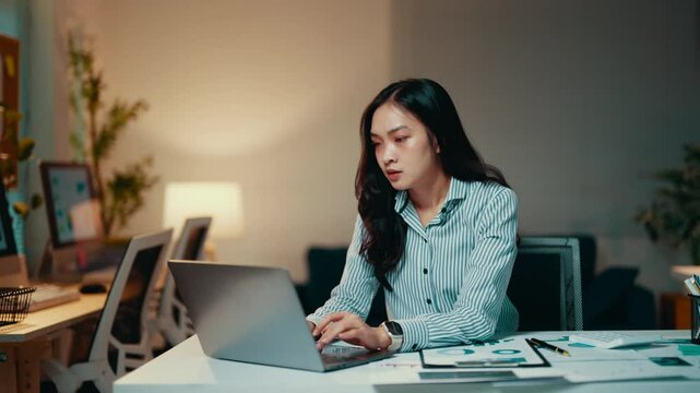 Young professional woman working late in the office. She is focused on her work but eventually becomes stressed and rubs her temples