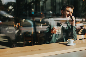 Toughtful man savoring coffee alone at a cozy cafe on a sunny day while lost in contemplation by the window