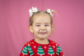 The child poses happily in a festive Christmas sweater, radiating joy and holiday spirit on a pink background. Perfect for greeting cards, banners and social media for Christmas and New Year.