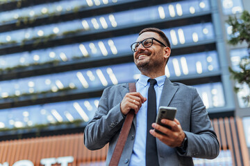 Confident Businessman Holding Smartphone Outside Modern Office Building