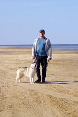 mature man with a husky dog stands on the seashore far from the city.