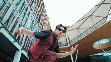 Low angle of asian attractive hipster pose at camera surround by mall. Portrait of break dance choreographer looking at camera while dancing in hip hop style. Outdoor sport 2024. Hiphop.