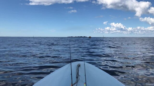 the bow of the boat is swinging, sailing on the sea waves, fishing rods are lying in the boat, sea fishing, white clouds in the blue sky above the sea, beautiful seascape