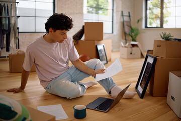 Young man doing taxes and using laptop while moving into new house.