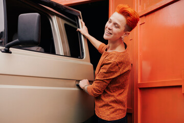 Smiling woman with vivid hair opening door of van near garage gate
