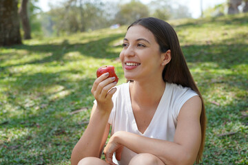 Brazilian healthy woman eating a red apple sitting in the city park
