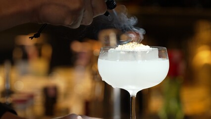 Closeup hand bartender using strainer in vodka coconut smooth fizzy cocktail at luxurious counter...