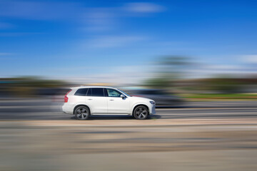 Fototapeta premium Fast moving car. A white SUV is driving on the highway at high speed on a blurred background