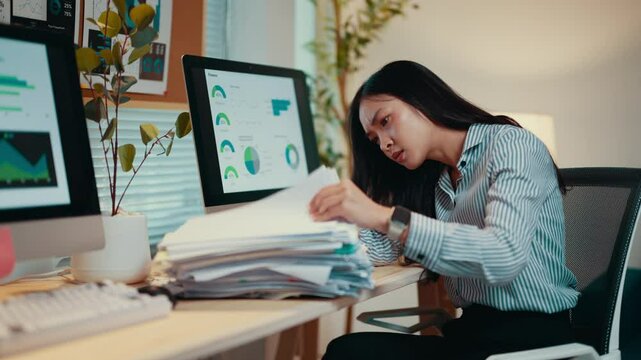 Asian businesswoman is getting increasingly frustrated with the amount of paperwork on her desk. She eventually gives up and rests her head on the desk