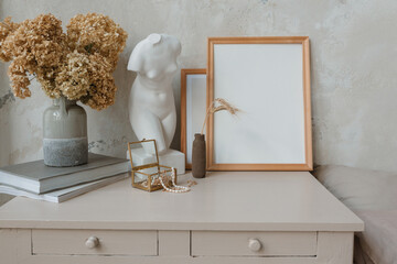 Blank picture frames next to a white statue, a vase with dried flowers and books along with...