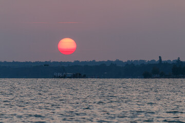 vibrant red sunrise over calm lake with distant silhouette
