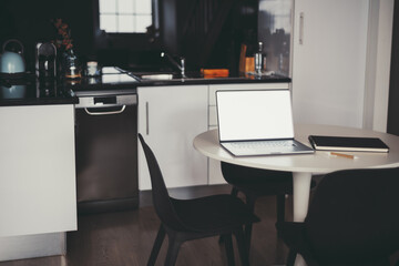 A minimalist kitchen workspace with a sleek laptop on a round table, accompanied by a notebook and pencil. Modern black and white decor, clean lines, and simple design elements
