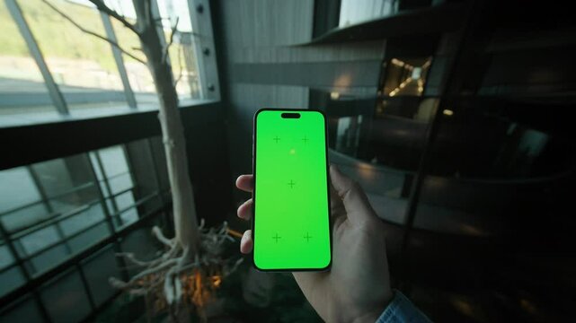 Close up hand man holding and scrolling vertically phone with green screen. On background cafe inside.. Typing on smartphone