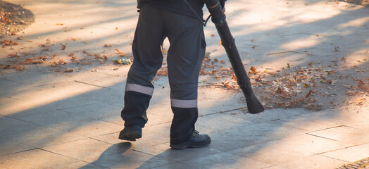 A man, a utility worker, removes leaves from the road with a special device.