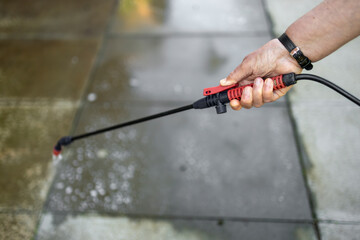 Spray gun with black plastic hose spraying liquid weed killer on gray concrete patio slabs