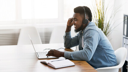 Customer support concept. Black millennial manager with headset using laptop in office, solving client's issue.