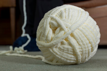Ball of chunky chenille crochet yarn with yarn on carpet floor and leading up out of frame to woman crocheting